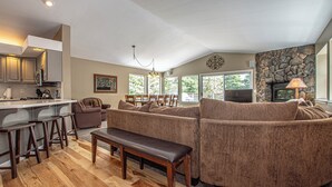 A spacious living area with a kitchen, a stone fireplace, and large windows. - Garret's Place by Hauserman Rental Group (Tahoe City)