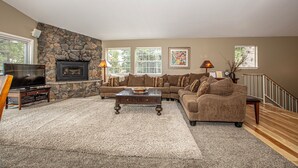 A living room with a stone fireplace, a television, a sofa, and a coffee table. - Garret's Place by Hauserman Rental Group (Tahoe City)