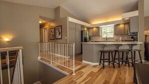 A modern kitchen with wooden flooring, a central island with stools, and a view to the dining area. - Garret's Place by Hauserman Rental Group (Tahoe City)