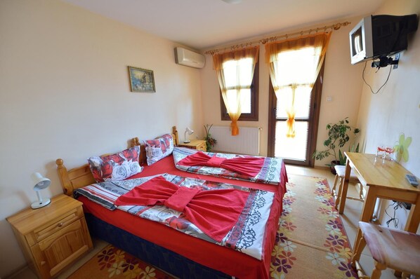 A bedroom with two beds, a desk, a chair, a TV, and a window with curtains. - Hotel Varusha (Veliko Tarnovo)