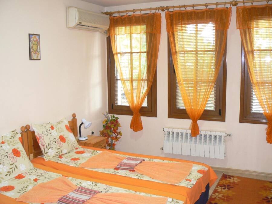 A bedroom with a bed, a nightstand, an air conditioner, a radiator, and curtains.