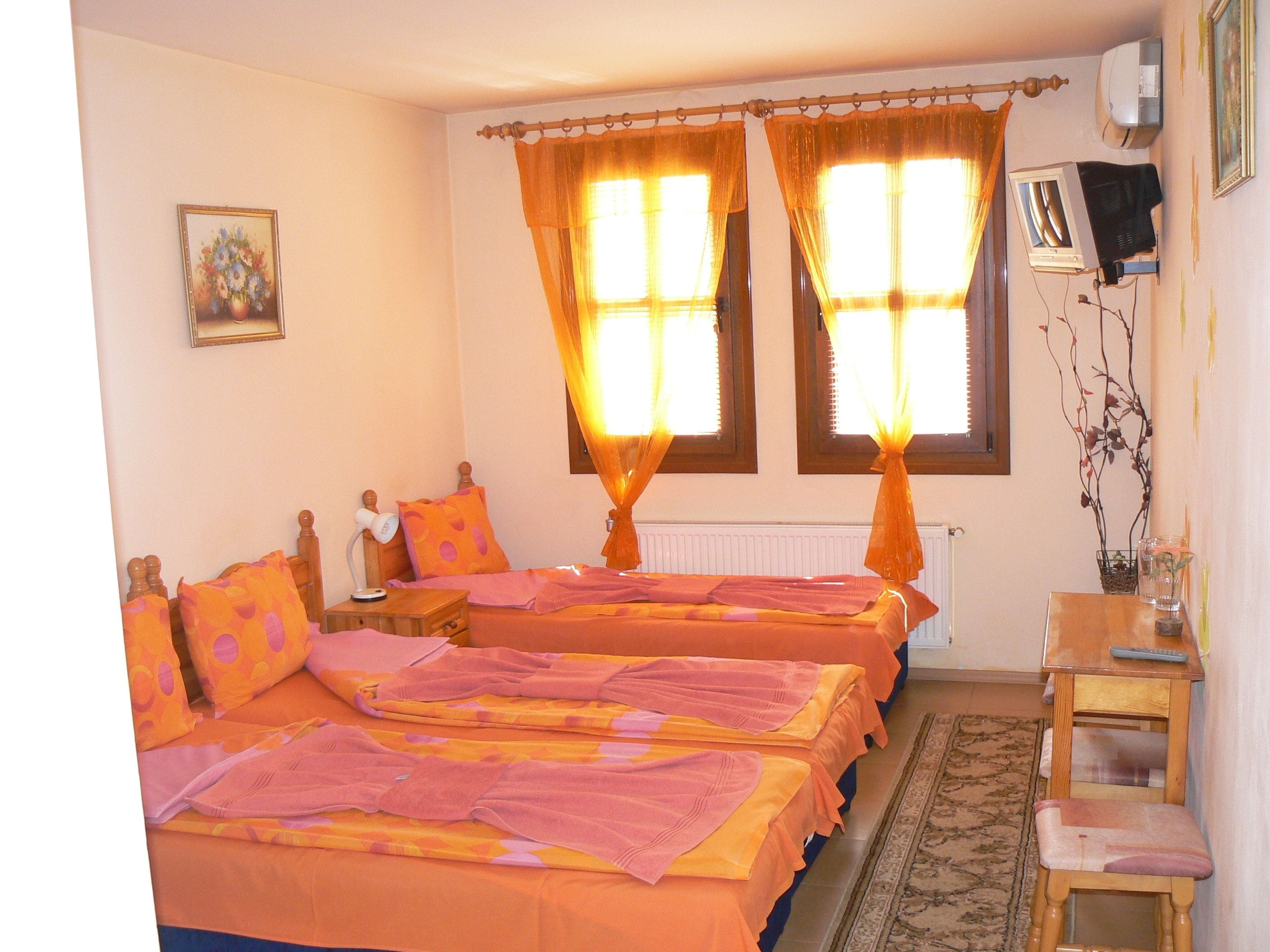 Una habitación con dos camas, una mesita de noche, una silla, un radiador y un televisor instalado en la pared.