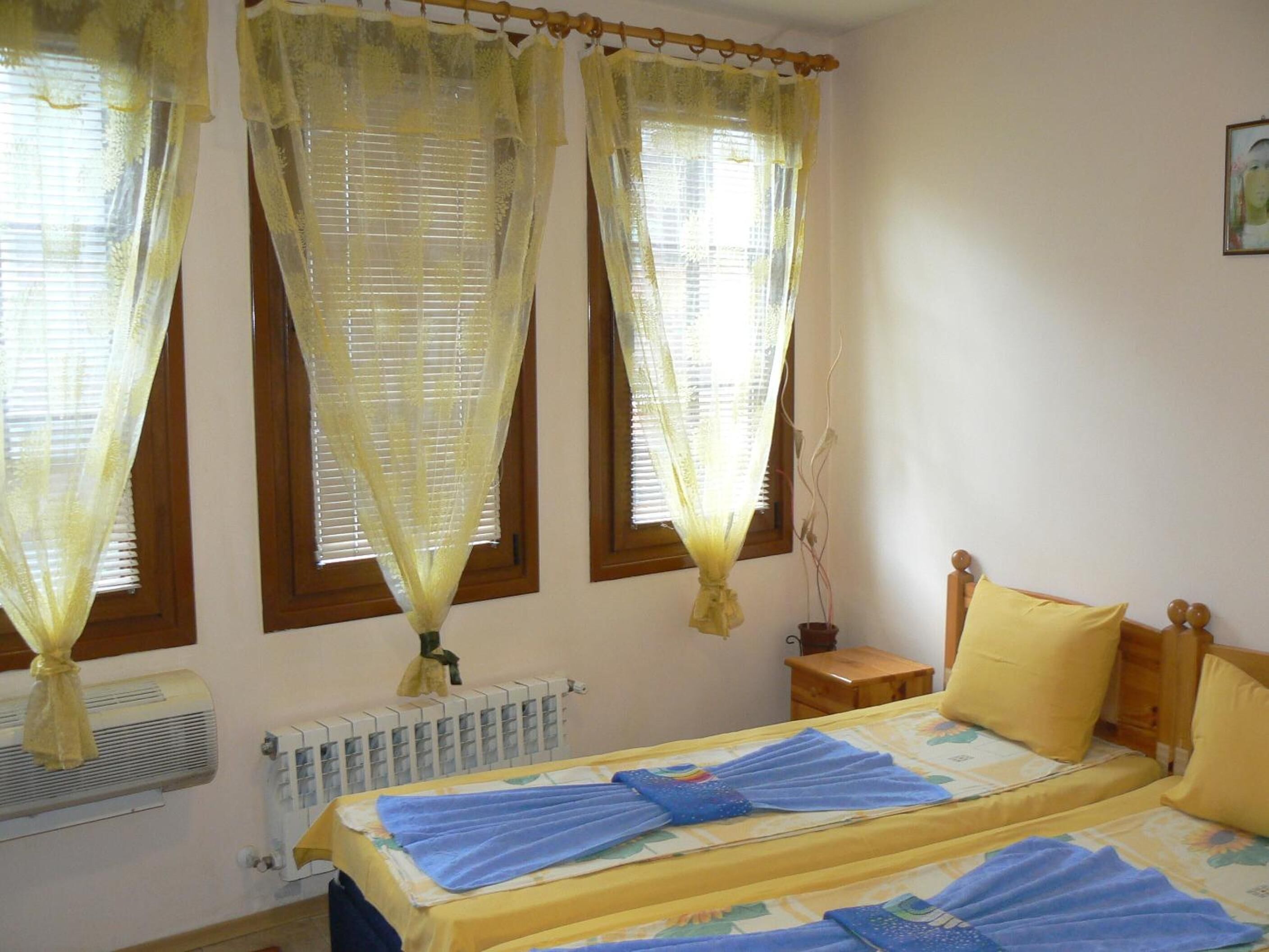 A bedroom with a bed, yellow curtains, a radiator, and a window with blinds.