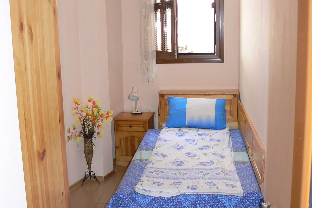 A bedroom with a bed, a nightstand, a window, and a radiator.