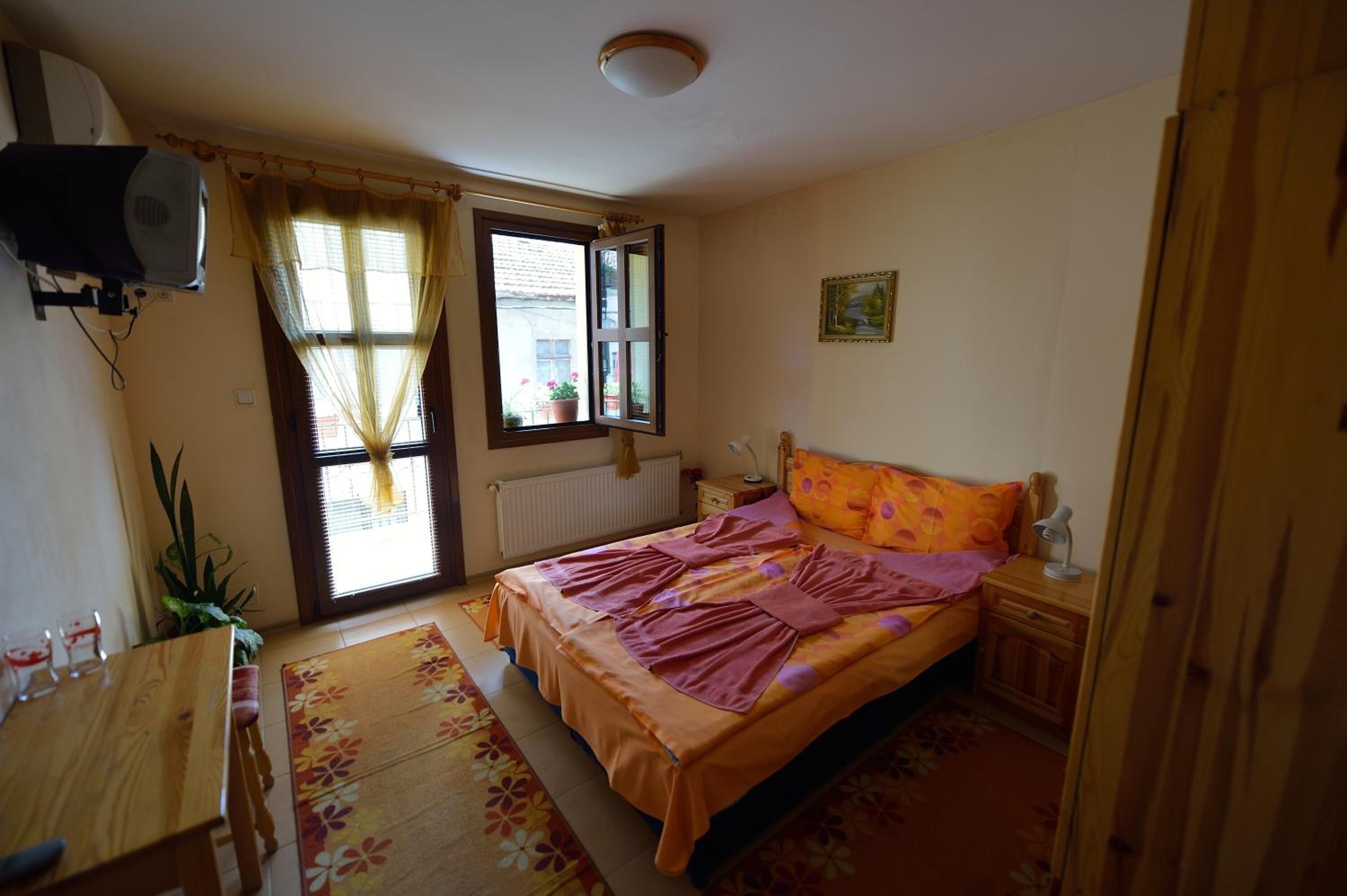 A bedroom with a bed, a window, a radiator, a desk, and a plant.