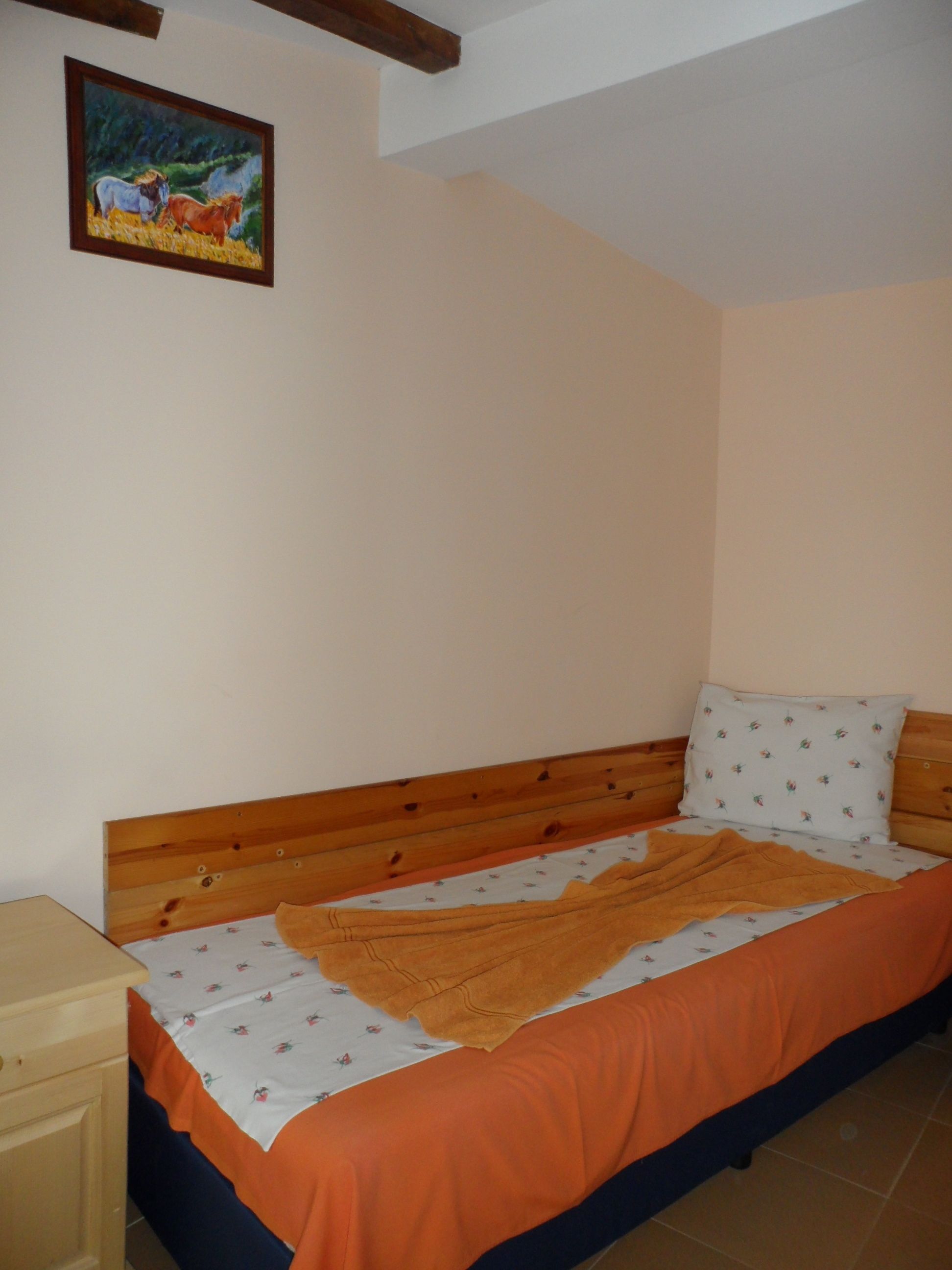 Een slaapkamer met een houten bed, een nachtkastje, een schilderij aan de muur en een raam.