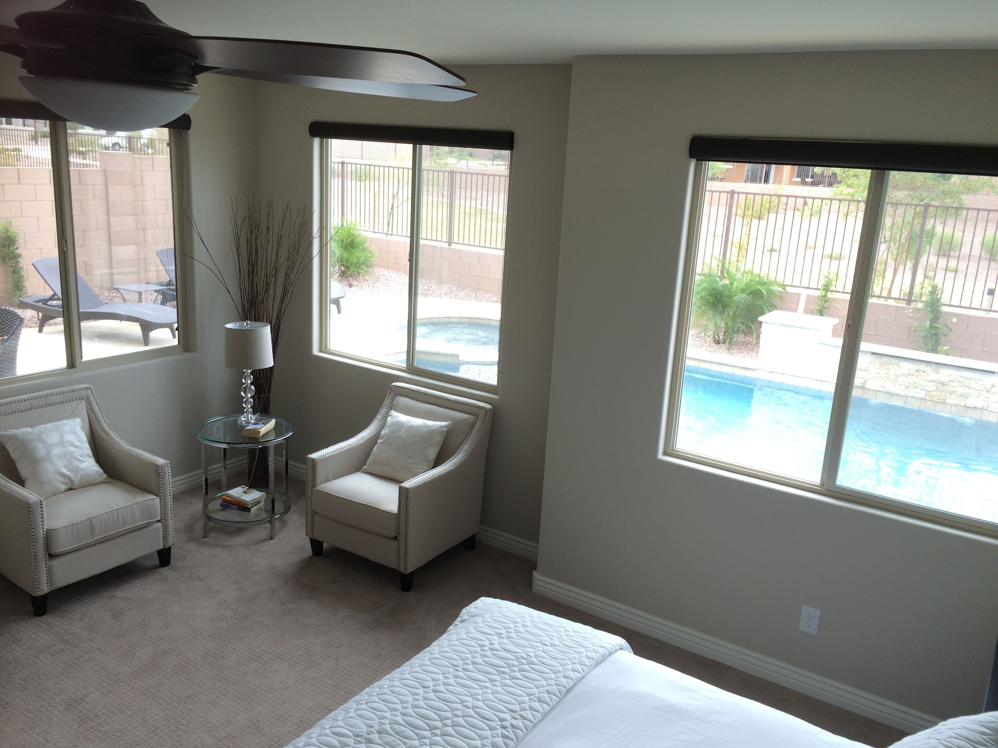 A bedroom with a large bed, two armchairs, a small table with a lamp, and a view of a swimming pool outside.