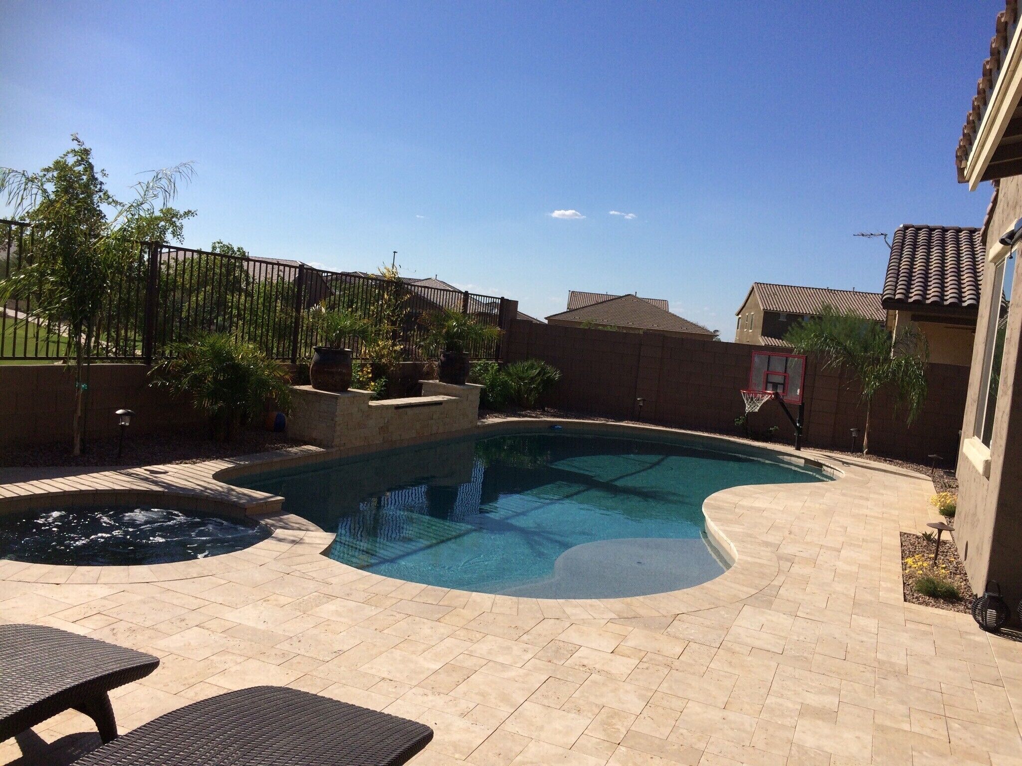 A backyard with a swimming pool, a hot tub, and a basketball hoop.