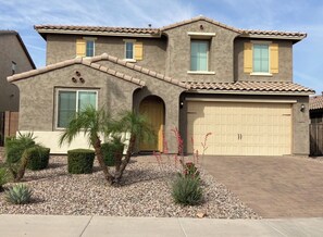 A two-story house with a garage, a small porch, and a landscaped front yard with plants and gravel.