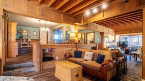 Un salón amplio con techo de madera, sofá de cuero, un cofre de madera y un televisor al fondo.