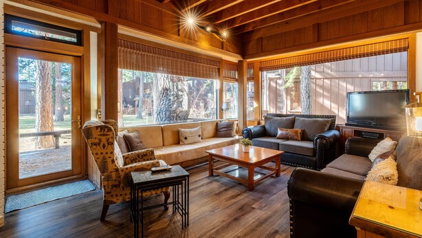 Un salón amplio con techo de madera, ventanas grandes, un sofá, una mesa de centro y un televisor.