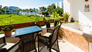 Ein Balkon mit Tisch und Stühlen, einer Badewanne und Blick auf Pool und Strand.