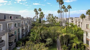A multi-story hotel with balconies, surrounded by palm trees and greenery.