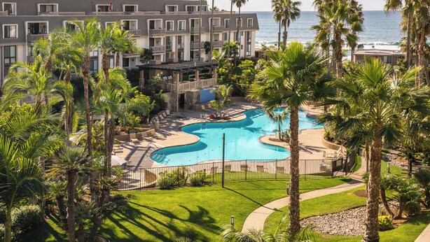 A resort with a swimming pool, palm trees, and a view of the ocean.