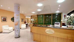 A hotel reception area with a wooden reception desk, a large pillar with a fish mural, and a few chairs. - Hotel Eurotel (Grottammare)
