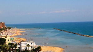 A coastal beach scene with a sandy shore, a pier extending into the sea, and buildings in the background. - Hotel Eurotel (Grottammare)