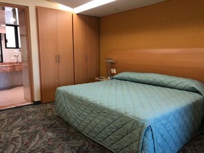 A hotel room with a bed, a wardrobe, a bedside table, and a lamp.