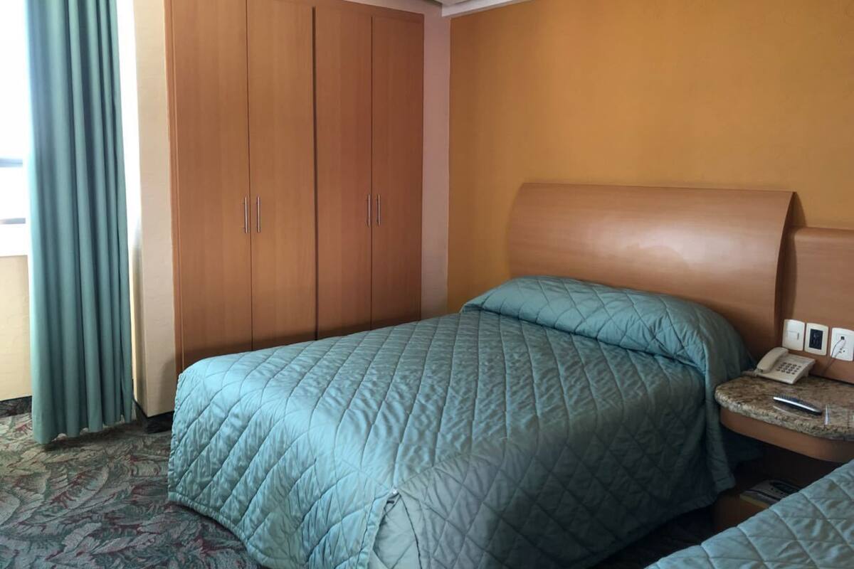 Een hotelkamer met een bed, een kledingkast, een nachtkastje met telefoon en een raam met gordijnen.