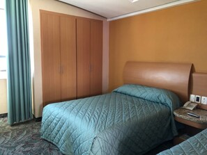 A hotel room with a bed, a wardrobe, a bedside table with a phone, and a window with curtains. - Hotel Plaza Las Fuentes (Puebla)