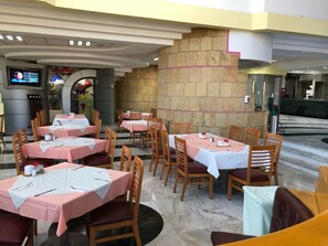 A restaurant with multiple tables and chairs, a stone wall, and a television screen.