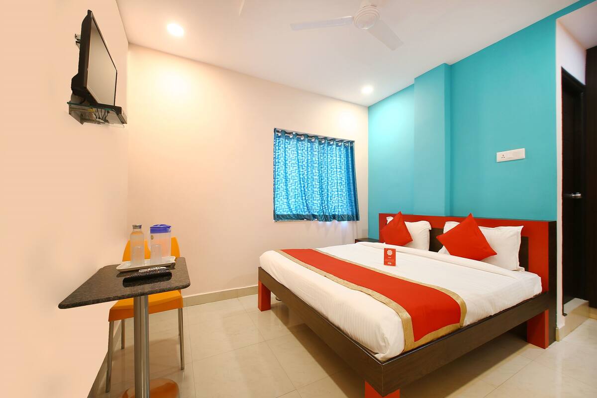Habitación de hotel con cama, escritorio con silla, ventana con cortinas y ventilador de techo.