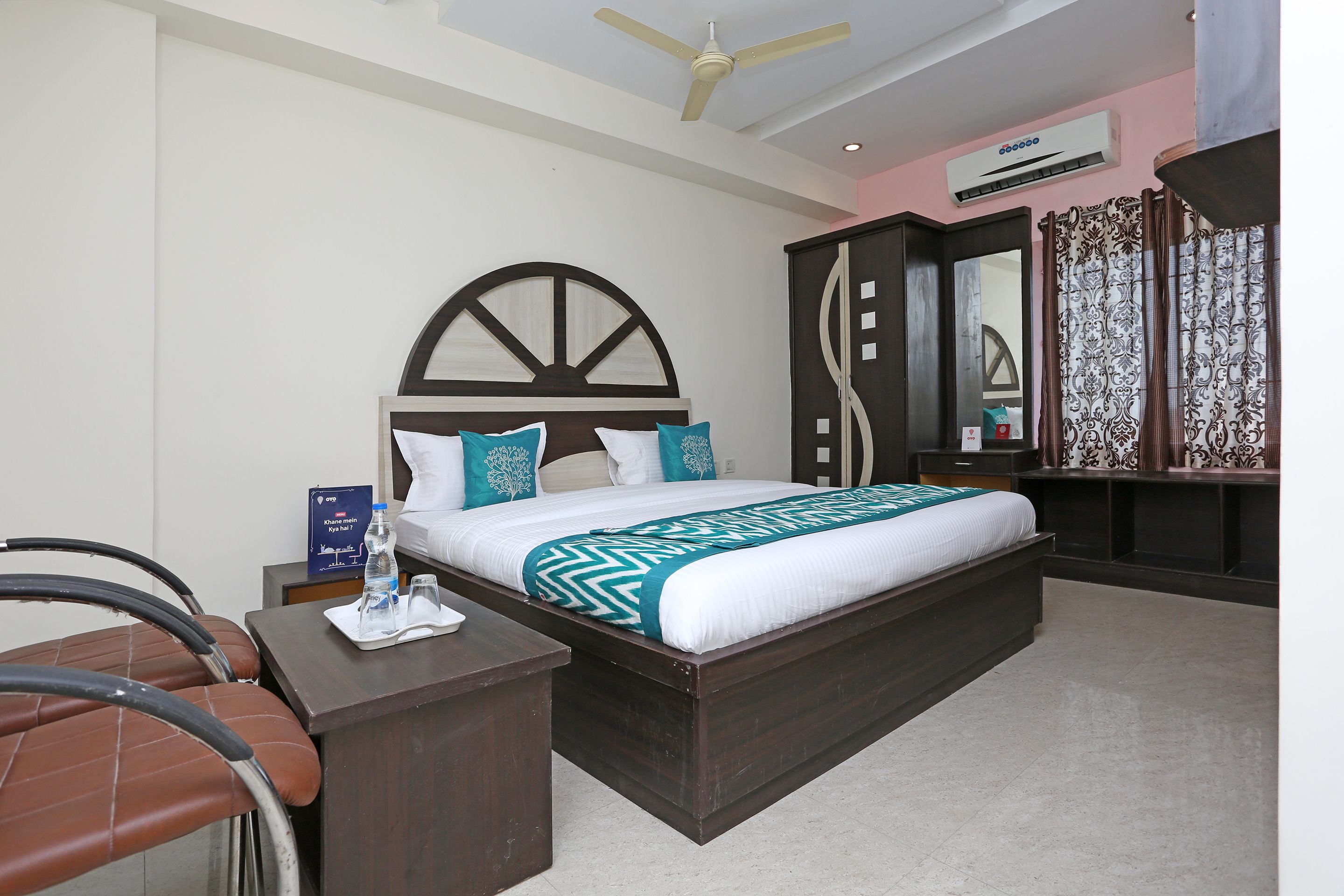 A hotel room with a large bed, a desk, a chair, and a ceiling fan.