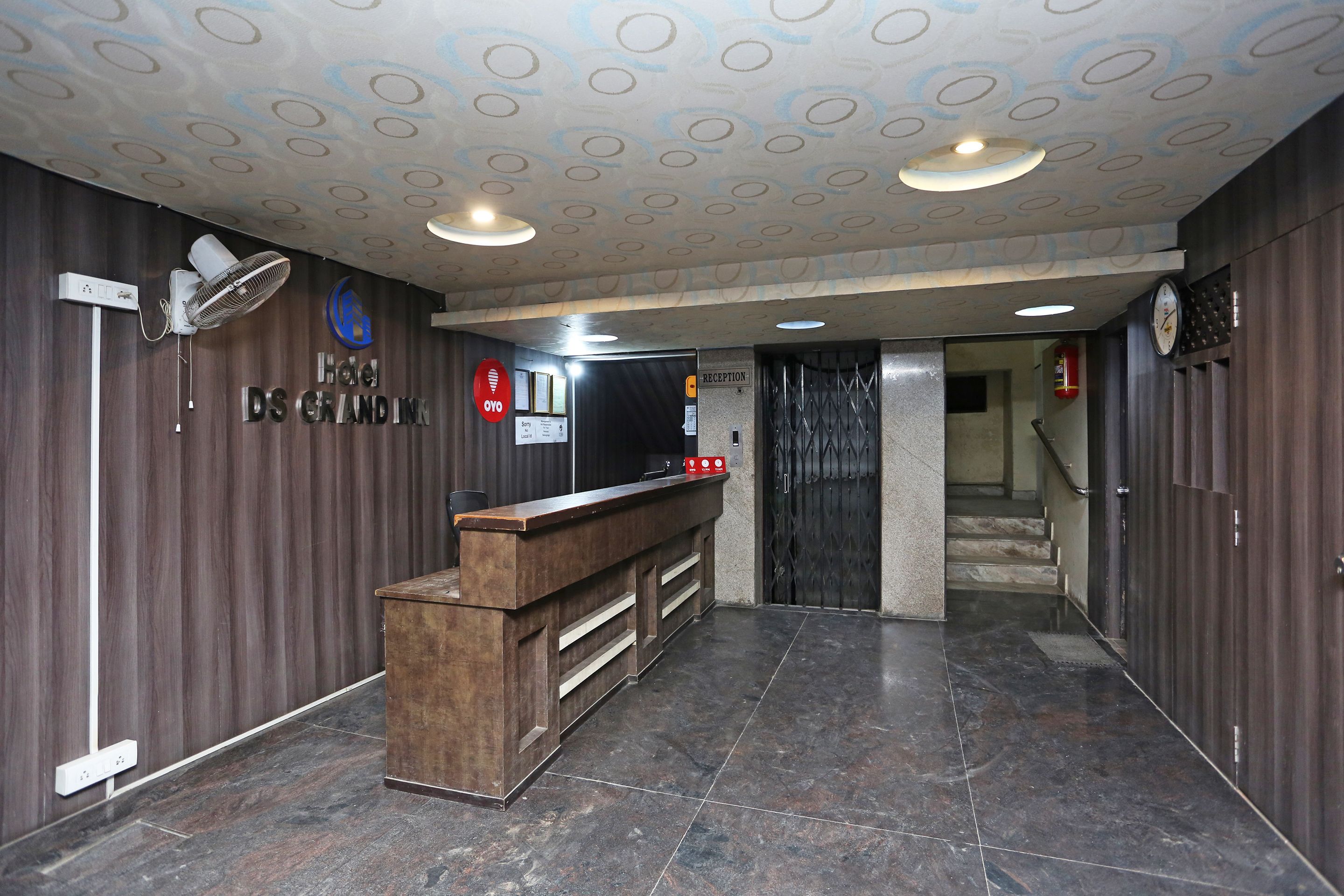 A hotel reception area with a wooden reception desk, a clock, and a reception sign.