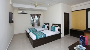 A hotel room with two beds, a ceiling fan, an air conditioning unit, a TV, and a small table with a water bottle and a brochure. - OYO 10188 Hotel DS Grand Inn (Ramachandrapuram)