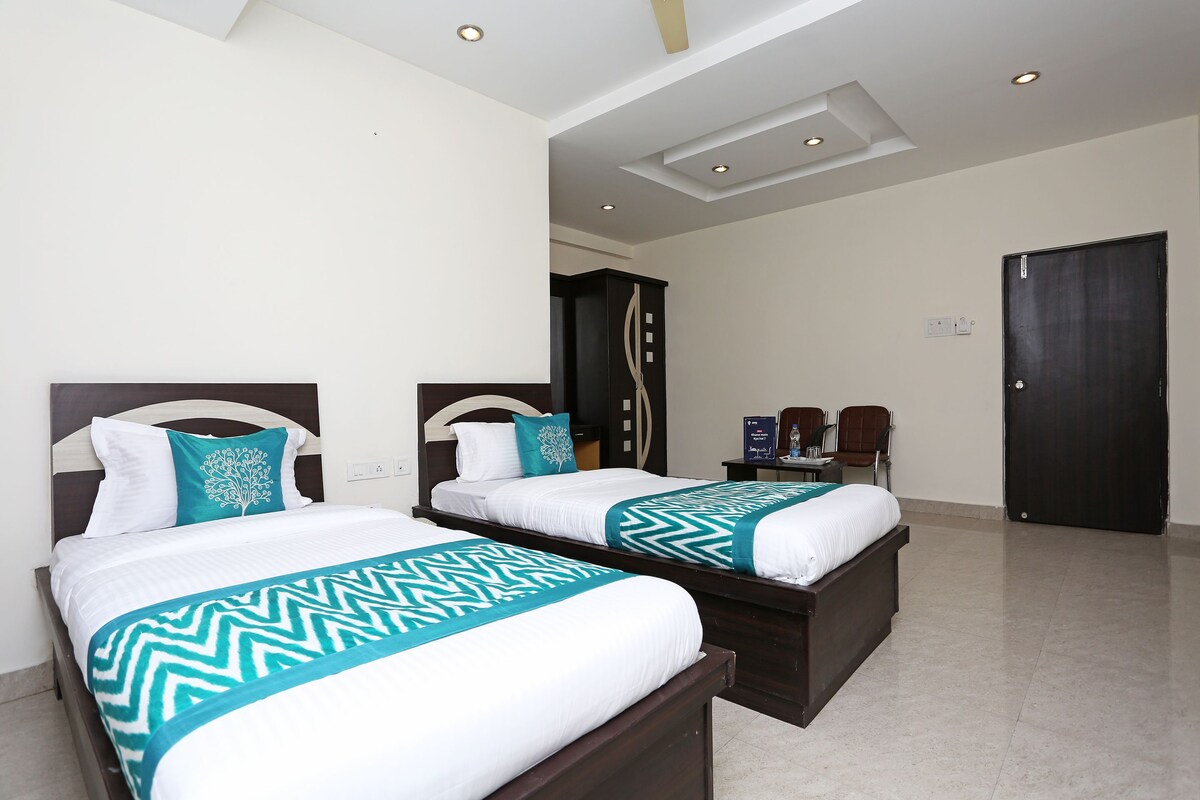 A hotel room with two beds, each with a white and teal bedspread, a wooden headboard, and a nightstand with a lamp.