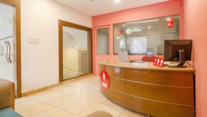 A reception area with a curved desk, a laptop, and a monitor. There are two windows with blinds, and a ceiling fan is visible. - OYO 10235 Oyster Transit Hotels (Hyderabad)