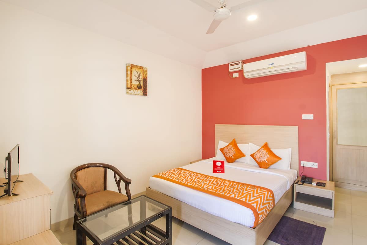 Habitación de hotel con cama, escritorio, silla, aire acondicionado y un cuadro en la pared.