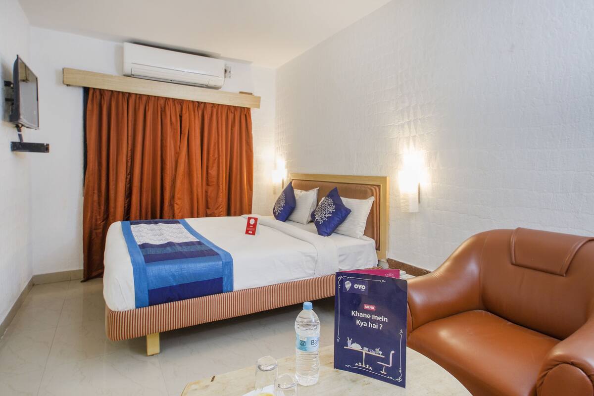 Una habitación de hotel con una cama, un sillón de cuero marrón, una botella de agua y un libro sobre la mesa.
