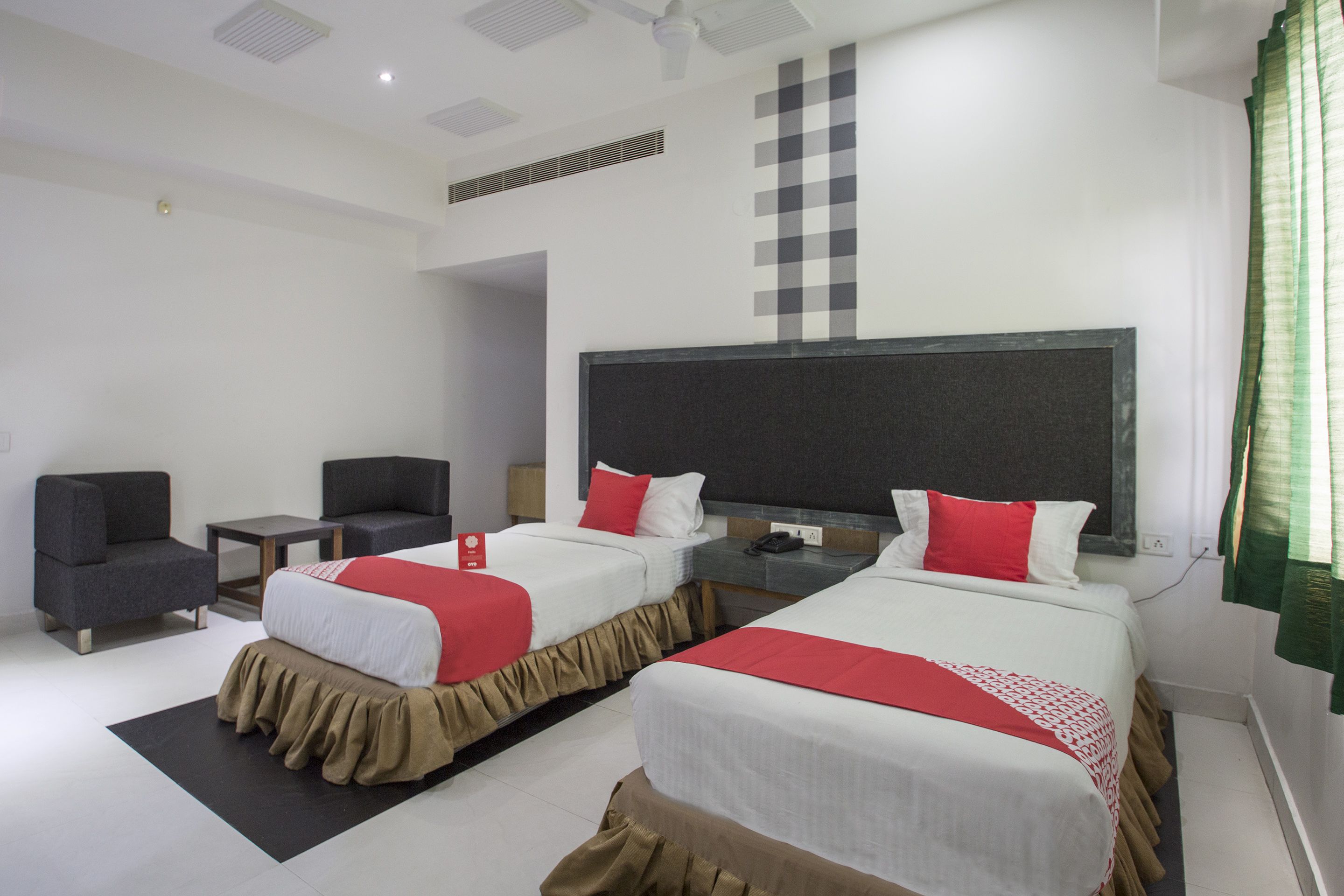A hotel room with two beds, a desk, a chair, and a large window with curtains.