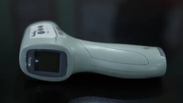 A handheld infrared thermometer with a digital display, a button, and a small screen.