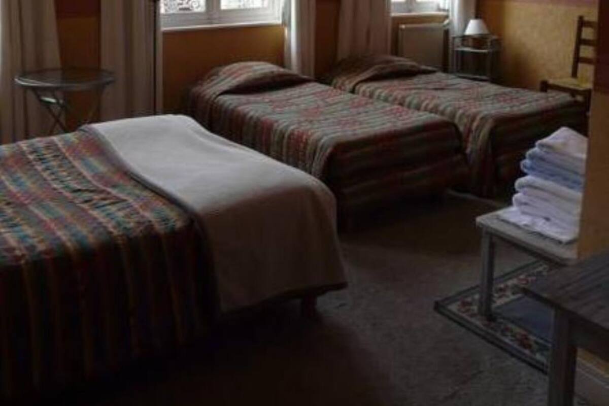 Habitación de hotel con dos camas, una mesita con toallas, una silla y una ventana con cortinas.