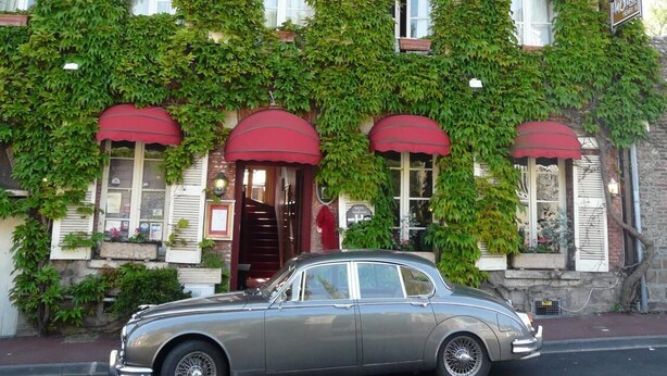Une voiture ancienne est garée devant un bâtiment recouvert de lierre vert.