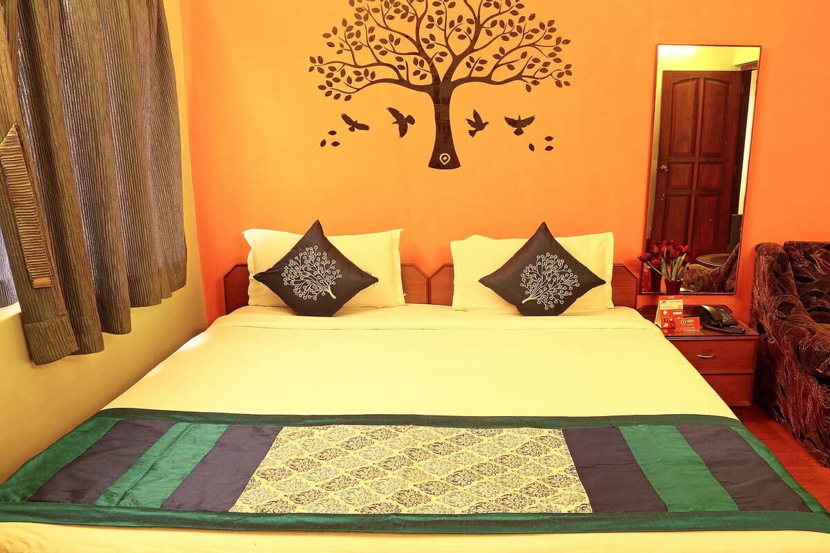 A bed with two decorative pillows, a bedside table with a phone and a vase of flowers, and a mirror on the wall.