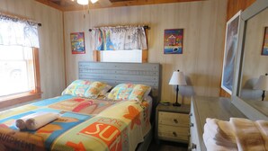 A bedroom with a bed, bedside tables, a nightstand, a lamp, and a window with curtains. - Summer Special/RIGHT ACROSS from OCEAN/Fenced yard/pet friendly  (Nags Head)
