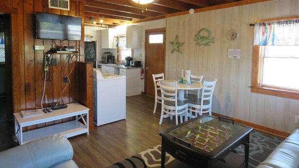A cozy living room with a foosball table, a TV, and a kitchen in the background. - Summer Special/RIGHT ACROSS from OCEAN/Fenced yard/pet friendly  (Nags Head)