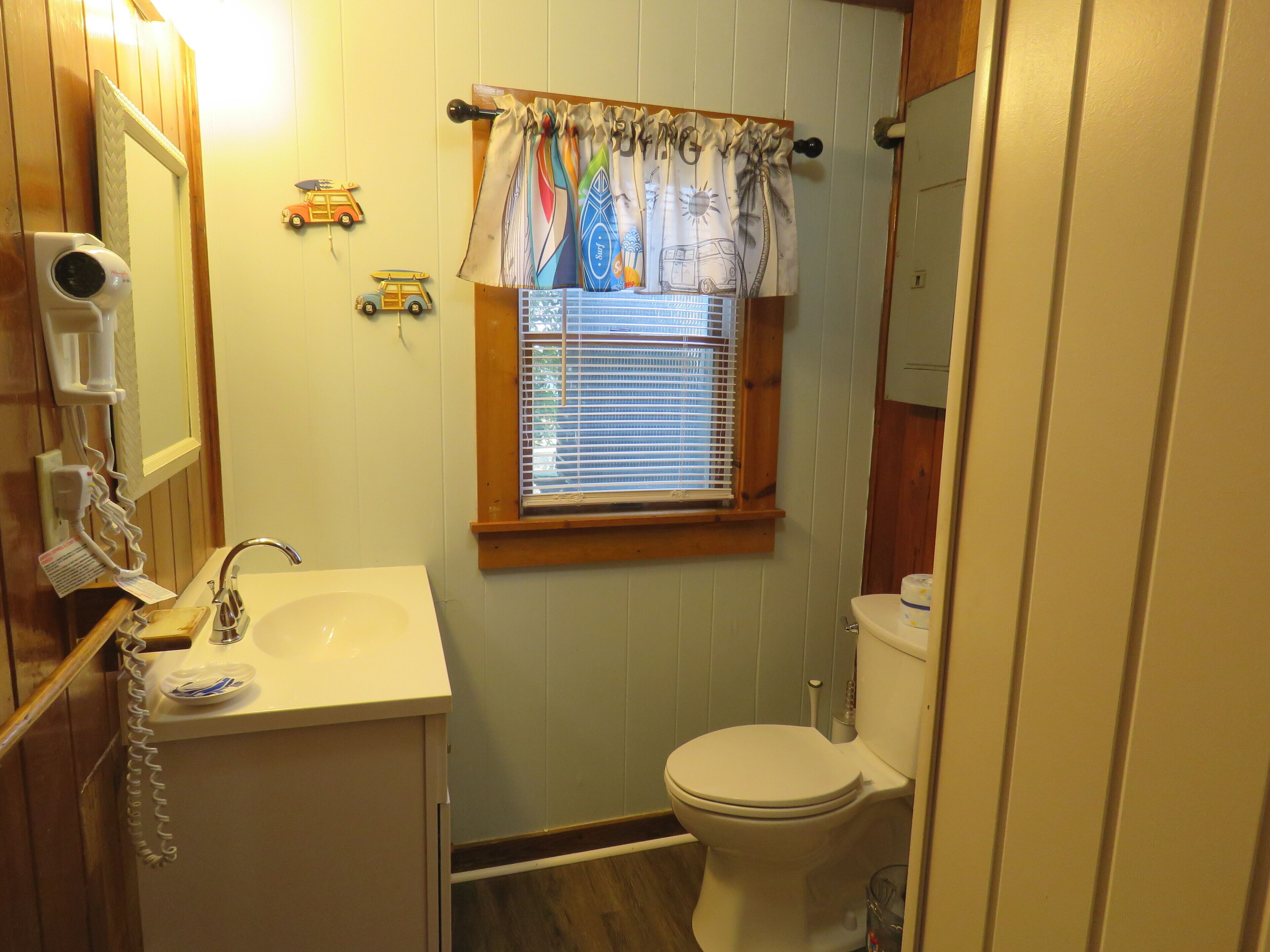 Ein kleines Badezimmer mit Waschbecken, Toilette und Fenster mit Jalousien.