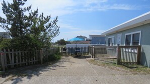 A gravel pathway leading to a building with a blue awning, surrounded by wooden fences and a tree. - Summer Special/RIGHT ACROSS from OCEAN/Fenced yard/pet friendly  (Nags Head)