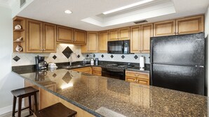 Una cocina con encimeras de granito, armarios de madera, un refrigerador negro y un microondas.