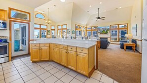 A spacious kitchen with a large island, wooden cabinets, and a view of the neighborhood through large windows. - Semi-Oceanfront Dog Friendly w/ Pool, Hot Tub, Home Theater, and Game Room (Avon)