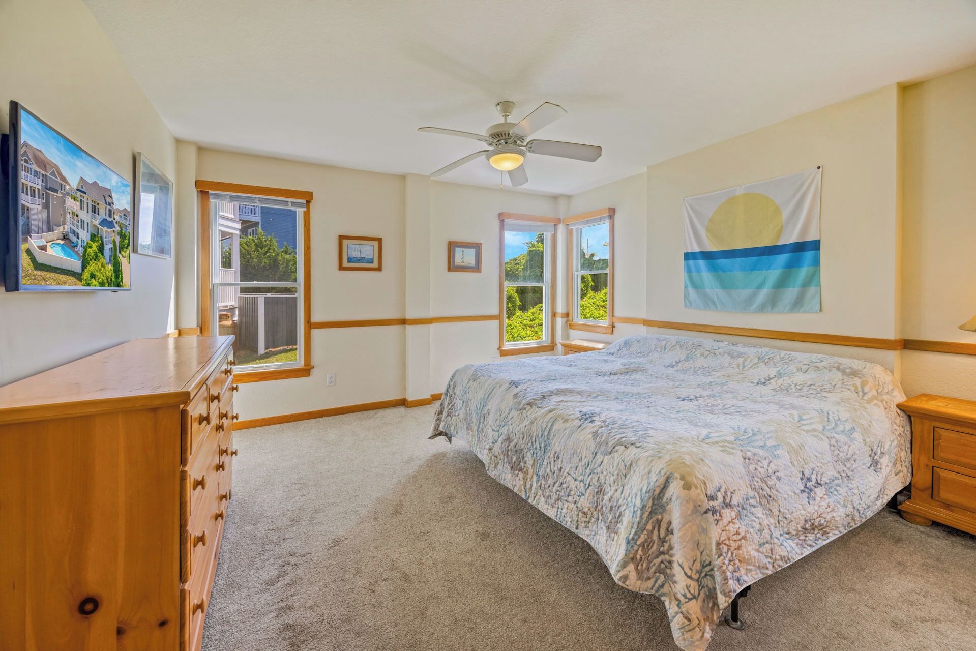 A bedroom with a bed, a dresser, a ceiling fan, a window with a view, and a flag on the wall.