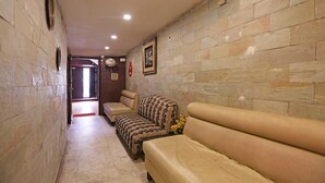 A corridor with stone walls, a framed picture, and a sofa with a patterned cover. - OYO 5048 Church View (Kolkata)