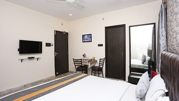 A hotel room with a bed, a TV mounted on the wall, a table with chairs, and a mirror. - OYO 5048 Church View (Kolkata)