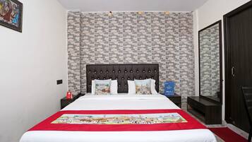 A neatly arranged hotel room with a large bed, a headboard, a nightstand, a dresser, a mirror, and a red carpet.