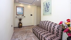A hallway with a patterned sofa, a ceiling fan, recessed lighting, a framed picture, and a decorative vase. - OYO 5048 Church View (Kolkata)