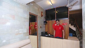 A hotel reception area with a wooden counter, a sofa, and a mirror reflecting the space. - OYO 5048 Church View (Kolkata)