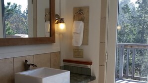 A bathroom with a large sink, wooden cabinets, a mirror, a towel rack, and a view of a balcony with trees. - Need to get away? This is your home away from - everything!
SEAGLASS Irish Beach (Manchester)